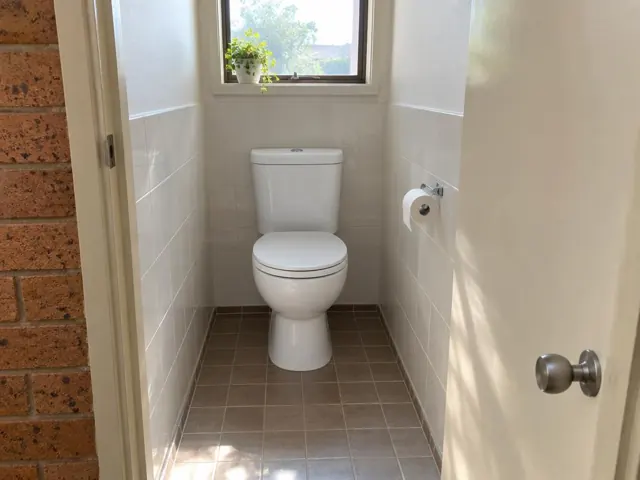 Clean white toilet in a tiled small bathroom with a window and brick doorway in Toongabbie