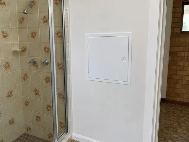 Small white access panel on a tiled shower wall beside a glass screen in Seven Hills